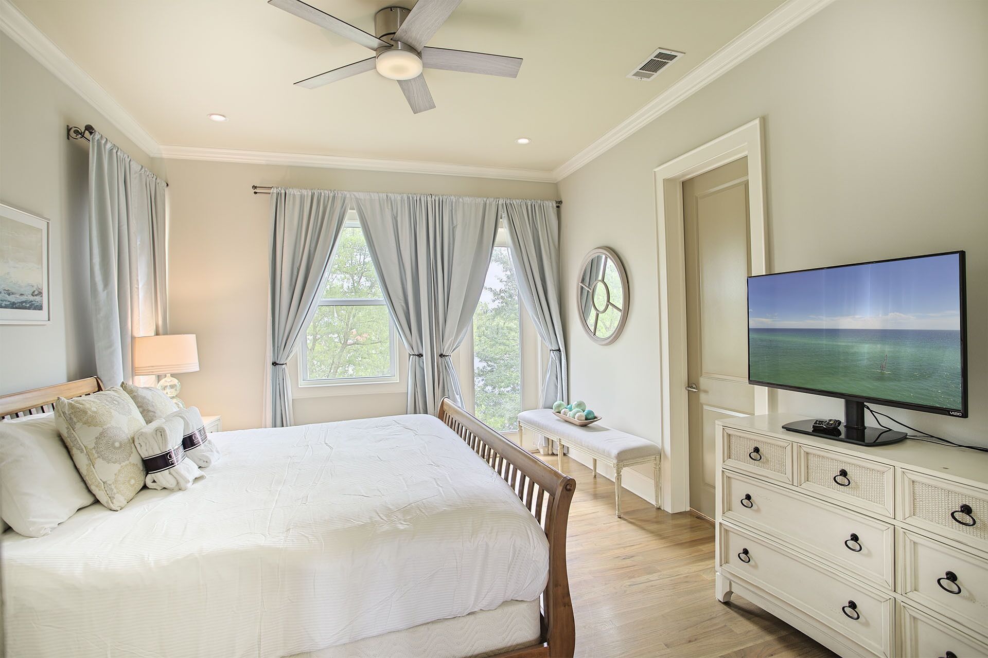 A bedroom with a bed, a dresser, a television, and a window with curtains.