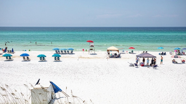 Una playa de arena blanca, agua turquesa cristalina y varias sombrillas y sillas de playa.