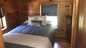 A wooden cabin bedroom with a bed, pillows, a window, and a small wooden cabinet.