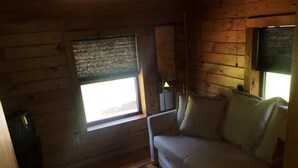 A cozy room with a wooden floor, a beige sofa, and a window with blinds.