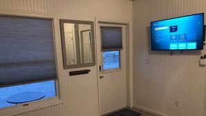 Una habitación con una televisión instalada en la pared, una puerta con un espejo y una ventana con vistas al exterior.