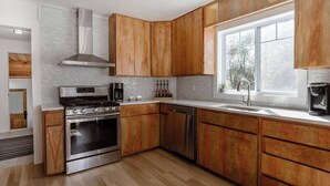 Une cuisine moderne avec des meubles en bois, une cuisinière en acier inoxydable et une fenêtre qui laisse entrer la lumière naturelle.