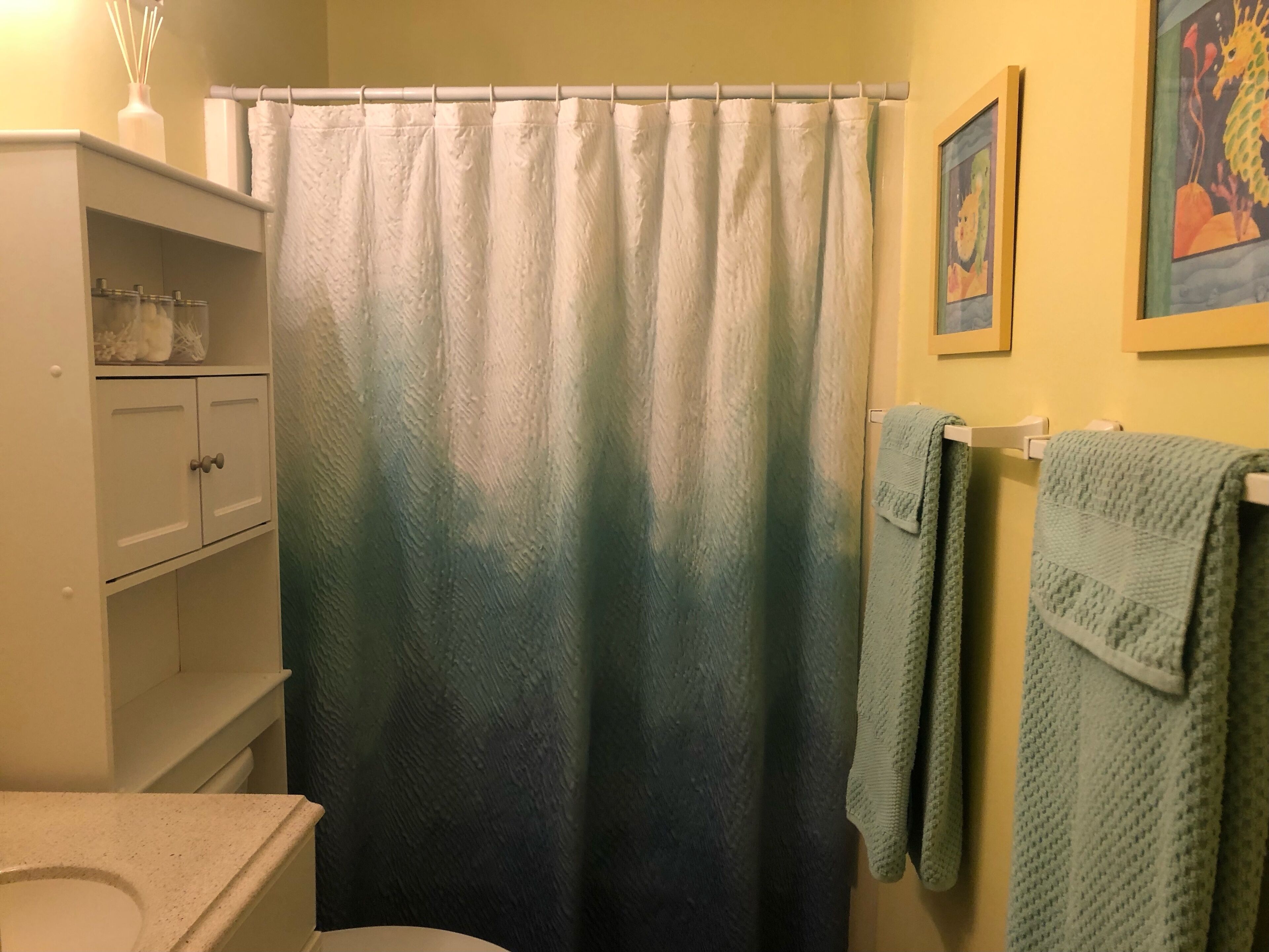 A bathroom with a shower curtain, a toilet, a sink, a cabinet, and towels on a rack.
