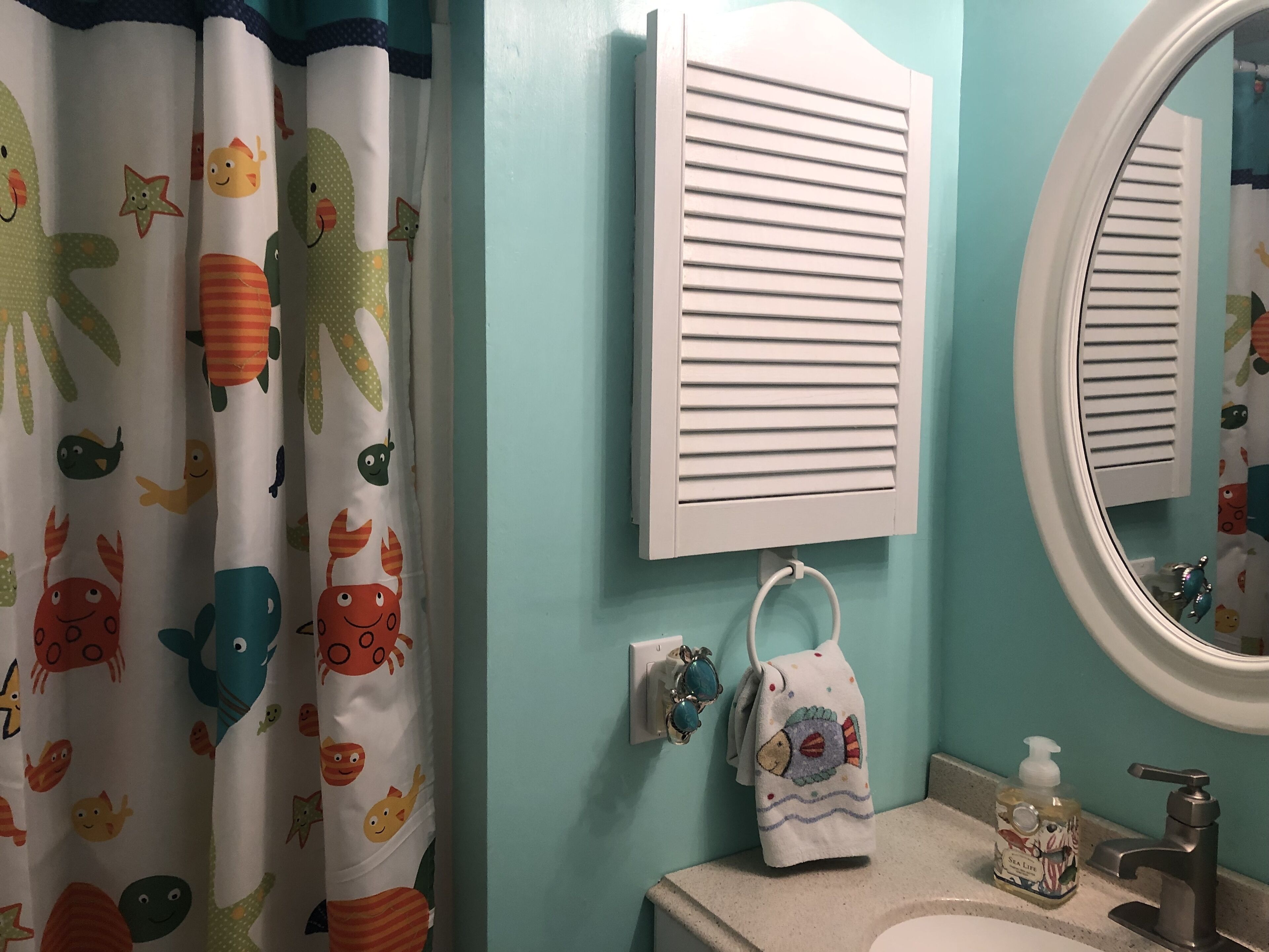 A bathroom with a teal wall, a white sink, a mirror, a towel rack with a towel, and a bottle of hand soap.