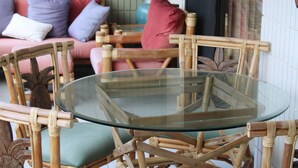 A room with a glass-top table surrounded by bamboo chairs with cushions. - Kona Ocean View:  Beautifully Furnished, Amazing View, White Sands Beach (Kailua-Kona)