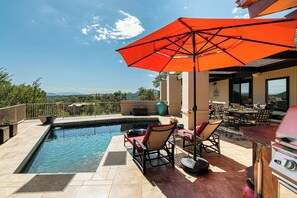 Uma área na piscina com churrasqueira, móveis de jardim e vista para a paisagem.
