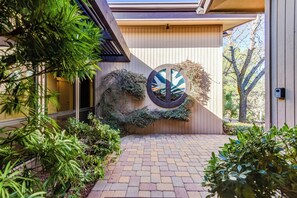 Uma casa moderna com um caminho de tijolos que leva a uma porta de madeira, rodeada por vegetação exuberante.