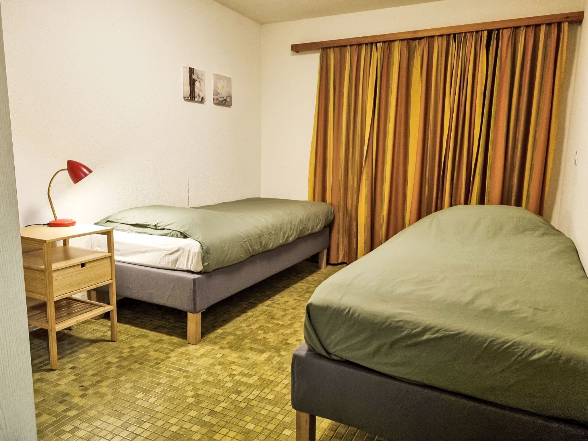 Ein Zimmer mit zwei Betten, einem Schreibtisch mit Lampe und einem Fenster mit Vorhängen.