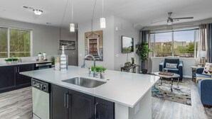 A modern kitchen with a central island, a dining area with a blue sofa, and a large window with a view. - Luxury King -TPC Shops Dining Close S200 (Phoenix)