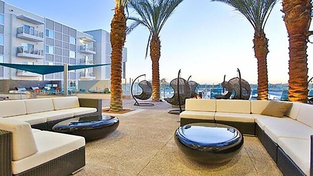 An outdoor seating area with sofas and round tables, palm trees, and a modern building in the background. - Luxury King -TPC Shops Dining Close S200 (Phoenix)