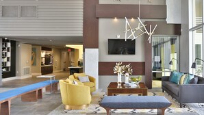 A modern lobby with a sofa, yellow armchair, and a bench. There is a wooden coffee table with a vase of flowers. - Luxury King -TPC Shops Dining Close S200 (Phoenix)