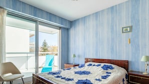 Un dormitorio con una cama grande, una silla, una mesita de noche y vistas al exterior.