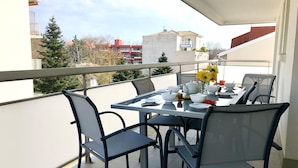 Un balcón con una mesa dispuesta para comer, sillas y un florero con flores.