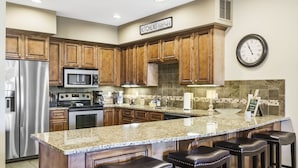 A kitchen with wooden cabinets, a stainless steel refrigerator, a microwave, a stove, and a large island with bar stools. - Spacious Branson Condo w/Pool, Elevator & Great Location Near All Attractions! (Branson)