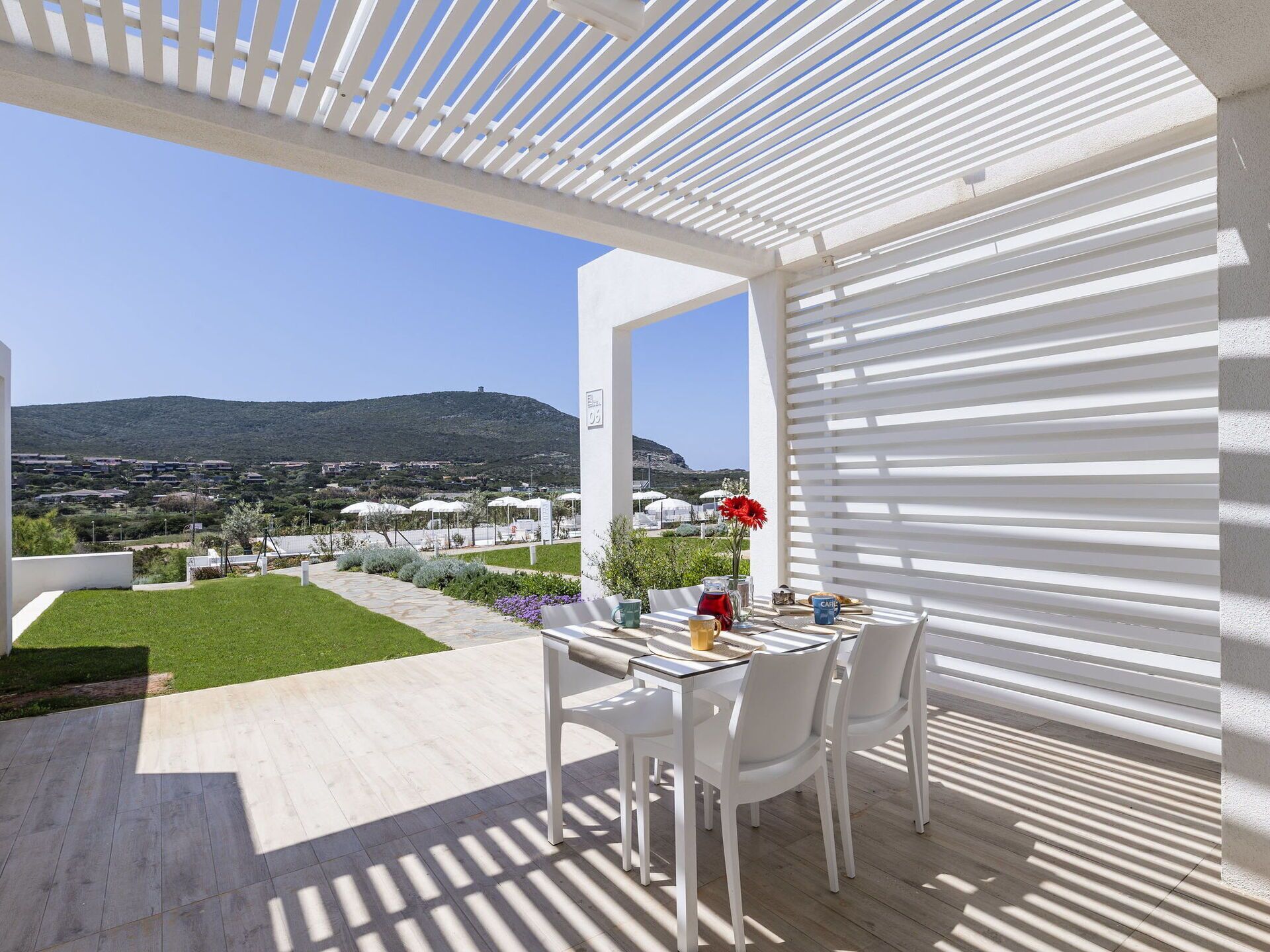 An outdoor patio with a table and chairs, a pergola, and a view of a hillside with buildings.