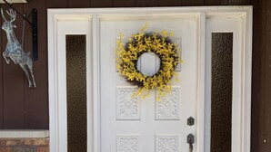 A white front door with a yellow wreath, a doormat with a message, and a metal deer decoration on the wall. - Country home with no pet fees!!  (Hillsboro)