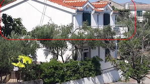 A white building with a red-tiled roof, surrounded by greenery and a concrete wall. - A 4 apt w big terrace, sea view & close to beach (Arbanija)