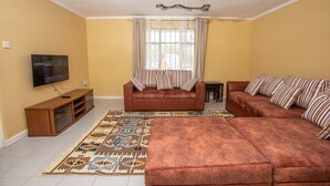 Ein Wohnzimmer mit einer Couch, Hocker, Fernseher und einem gemusterten Teppich.