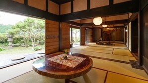 A traditional Japanese room with tatami flooring, a wooden table with a decorative mat, and a view of a garden with a stone lantern. - The Ninja Mansion (Toyota)