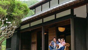 A traditional wooden building with a porch, large windows, and a tree with hanging lanterns. - The Ninja Mansion (Toyota)
