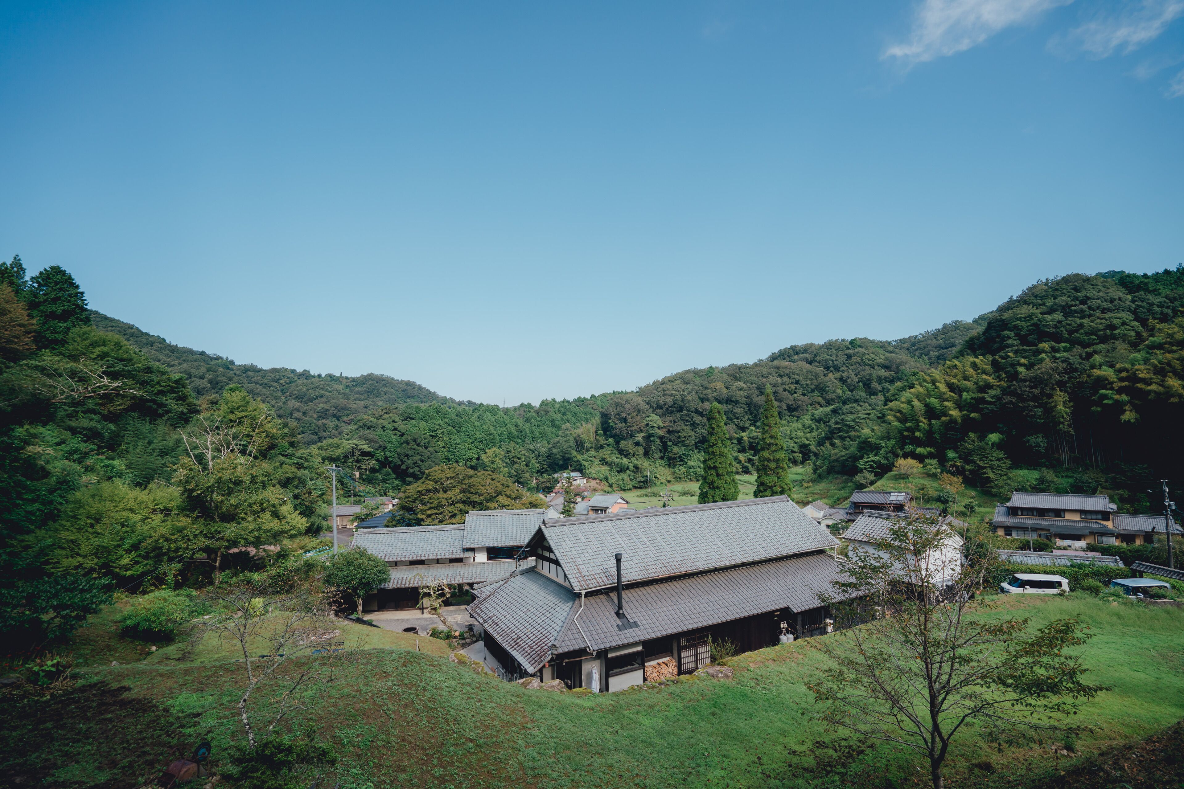 A traditional Japanese village with multiple buildings, surrounded by lush greenery and hills.