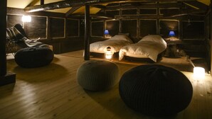 A cozy, dimly lit room with two beds, a lounge chair, and a wooden floor. - The Ninja Mansion (Toyota)