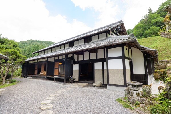 Un edificio japonés tradicional con tejado de tejas, vigas de madera y un camino de grava que conduce a la entrada.