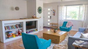 A living room with a TV, bookshelves, a coffee table, and two chairs. - Spacious Duplex with 3 King Beds ★ Conveniently Located Near AFA (Colorado Springs)