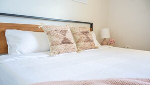 A neatly made bed with white bedding and two patterned pillows, a wooden headboard, a bedside lamp, and a small vase with flowers on the nightstand. - Spacious Duplex with 3 King Beds ★ Conveniently Located Near AFA (Colorado Springs)
