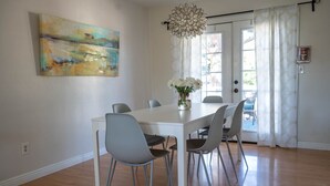 A dining area with a white table and grey chairs, a vase with white flowers, and a painting on the wall. - Spacious Duplex with 3 King Beds ★ Conveniently Located Near AFA (Colorado Springs)