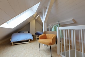 A loft bedroom with a sloped ceiling, a bed, an orange chair, and a white crib. - Comfortable Vacation Apartment "Goldener Mond" with Wi-Fi, Balcony (Mastershausen)
