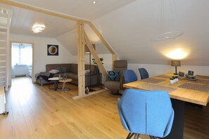 A spacious loft-style living area with a high ceiling, wooden beams, a dining table with chairs, a sofa, and a staircase. - Comfortable Vacation Apartment "Goldener Mond" with Wi-Fi, Balcony (Mastershausen)