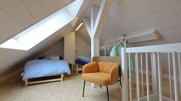 Une chambre à coucher aménagée dans un espace mansardé, avec un plafond en pente, un lit, un fauteuil orange et un berceau blanc.