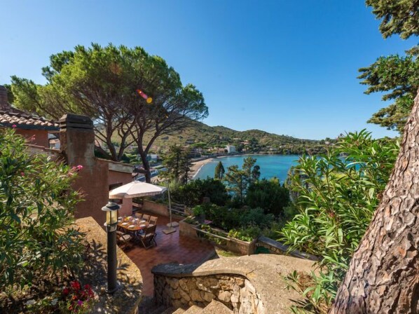 A patio with outdoor furniture, a stone wall, and a view of a coastal landscape.