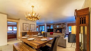 Un comedor con una mesa de madera dispuesta para cuatro personas, un candelabro y una chimenea de piedra al fondo.