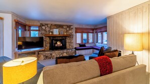 Una sala de estar acogedora con chimenea de piedra, televisor de pantalla plana, sofá y un asiento junto a la ventana.