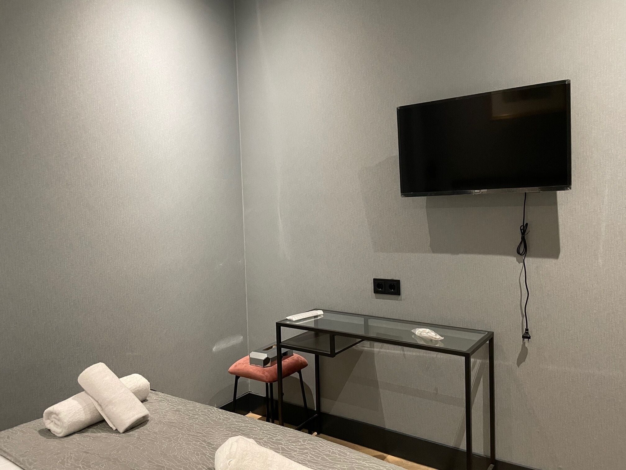 A modern hotel room with a bed, a desk, a television mounted on the wall, and a pair of towels on the bed.