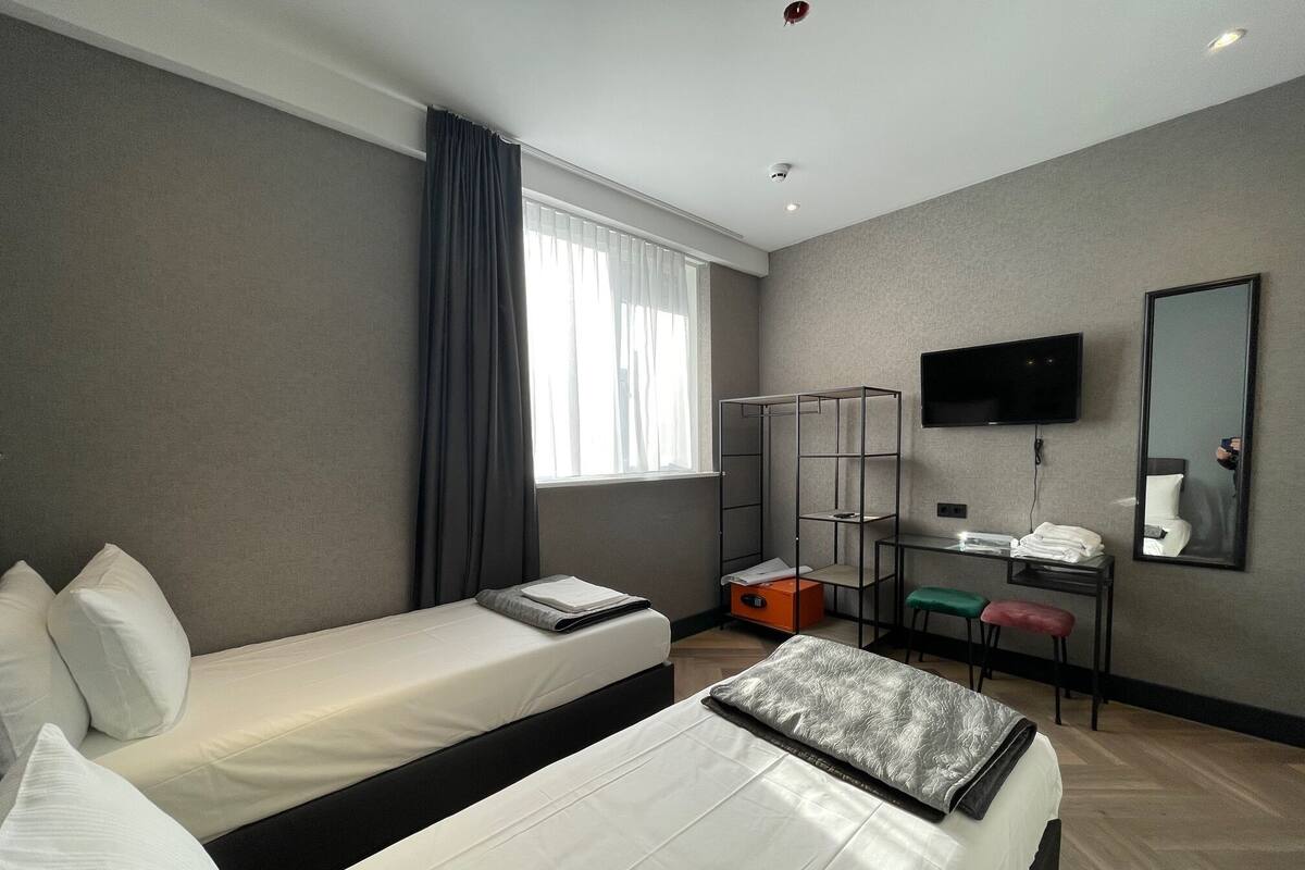 A hotel room with two beds, a desk, a chair, a TV, and a wardrobe.