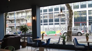 A cafe with tables and chairs, large windows, and potted plants. - H3 Hotel Rotterdam City Center (Rotterdam)