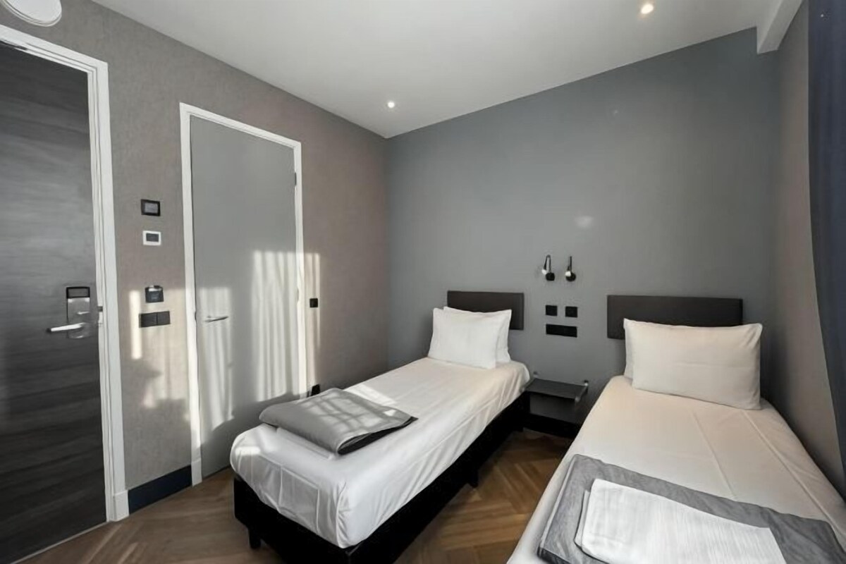 A hotel room with two beds, a door, and a wall-mounted light fixture.