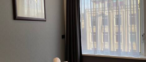 A hotel room with a bed, a window with sheer curtains, and a framed picture on the wall.