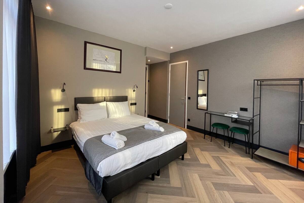 A hotel room with a bed, bedside tables, a desk, a chair, and a mirror.