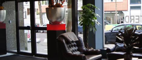 A lobby with a checkered floor, a leather sofa, a potted plant, and a large metal bowl with flowers.
