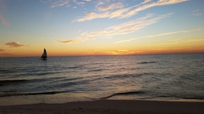 Une scène de plage avec un voilier sur l’eau au coucher du soleil.