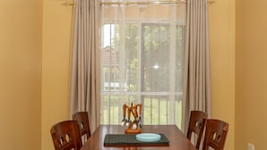 A dining room with a wooden table and chairs, a chandelier, and a window with curtains. - Cozy and Warm 3-bed Bungalow in Athi River (Athi River)