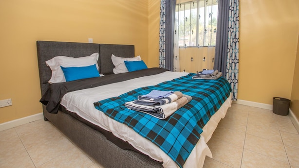 A neatly made bed with a blue and black checkered bedspread, two pillows, and a folded towel on the bed. - Cozy and Warm 3-bed Bungalow in Athi River (Athi River)