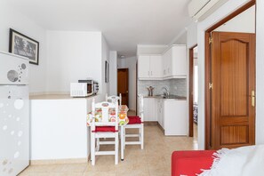 A compact kitchen with white appliances, a dining table with chairs, and a red sofa.