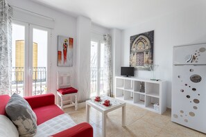 A modern living room with a red sofa, a white coffee table, a TV, and a decorative wall piece.