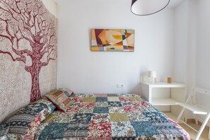 Ein Schlafzimmer mit gesteppter Bettdecke, Wandteppich, Gemälde, weißem Schreibtisch und Stuhl.