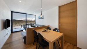 Un comedor moderno con una mesa de madera, sillas negras y vistas a montañas a través de amplios ventanales.